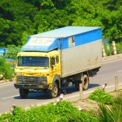 pexels-photo-13040619-13040619 Colorful truck drives on a sunny Chattogram road, surrounded by greenery.